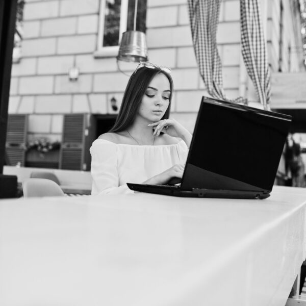 Portrait of a strong independent successful businesswoman wearing smart casual clothing and glasses working on a laptop in a cafe. Black and white photo.